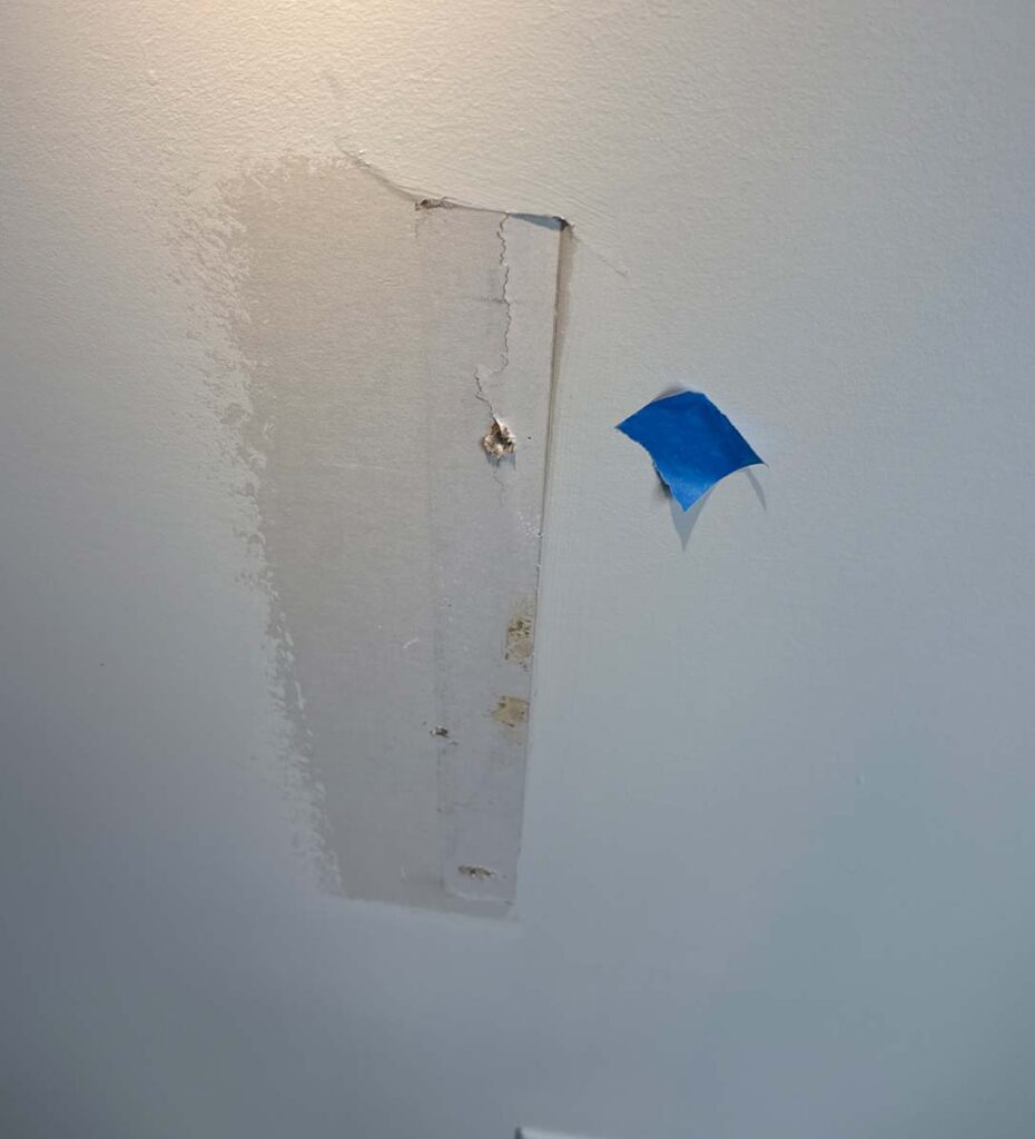 Interior wall showing an unfinished drywall repair with visible cracks, damaged plaster, and uneven paint around the patched area.