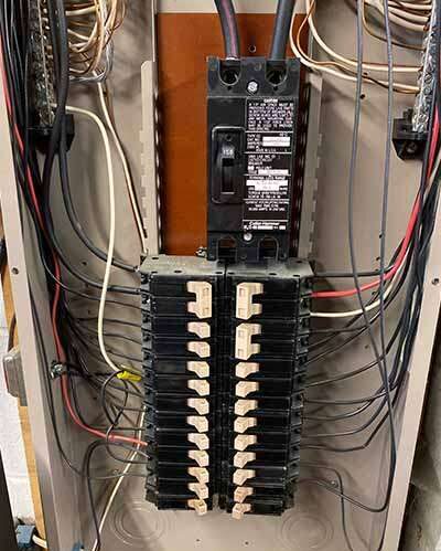 Open residential electrical service panel showing the main breaker, branch circuit breakers, and visible wiring during a home inspection.