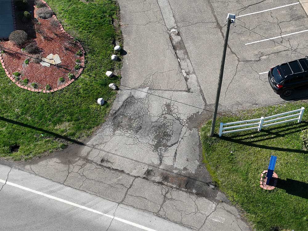 Aerial view of commercial asphalt pavement showing cracking, deteriorated surfaces, and previously repaired areas.