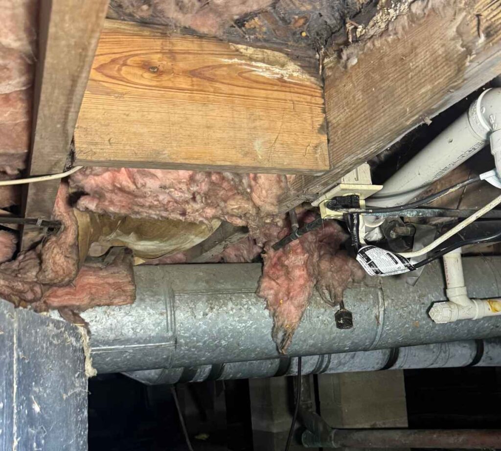 Sagging and loose fiberglass insulation hanging beneath wooden floor joists in a residential crawl space, with exposed HVAC ductwork and plumbing.