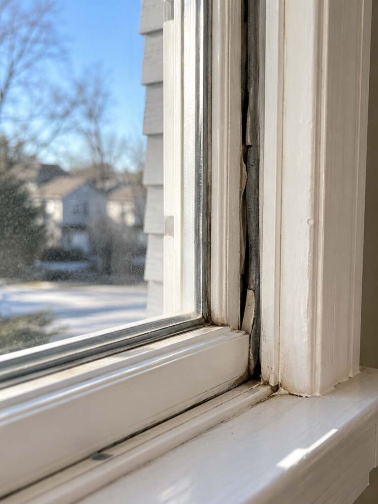 Close-up of a residential window showing cracked and deteriorated weatherstripping with visible gaps that may allow drafts and air leakage.