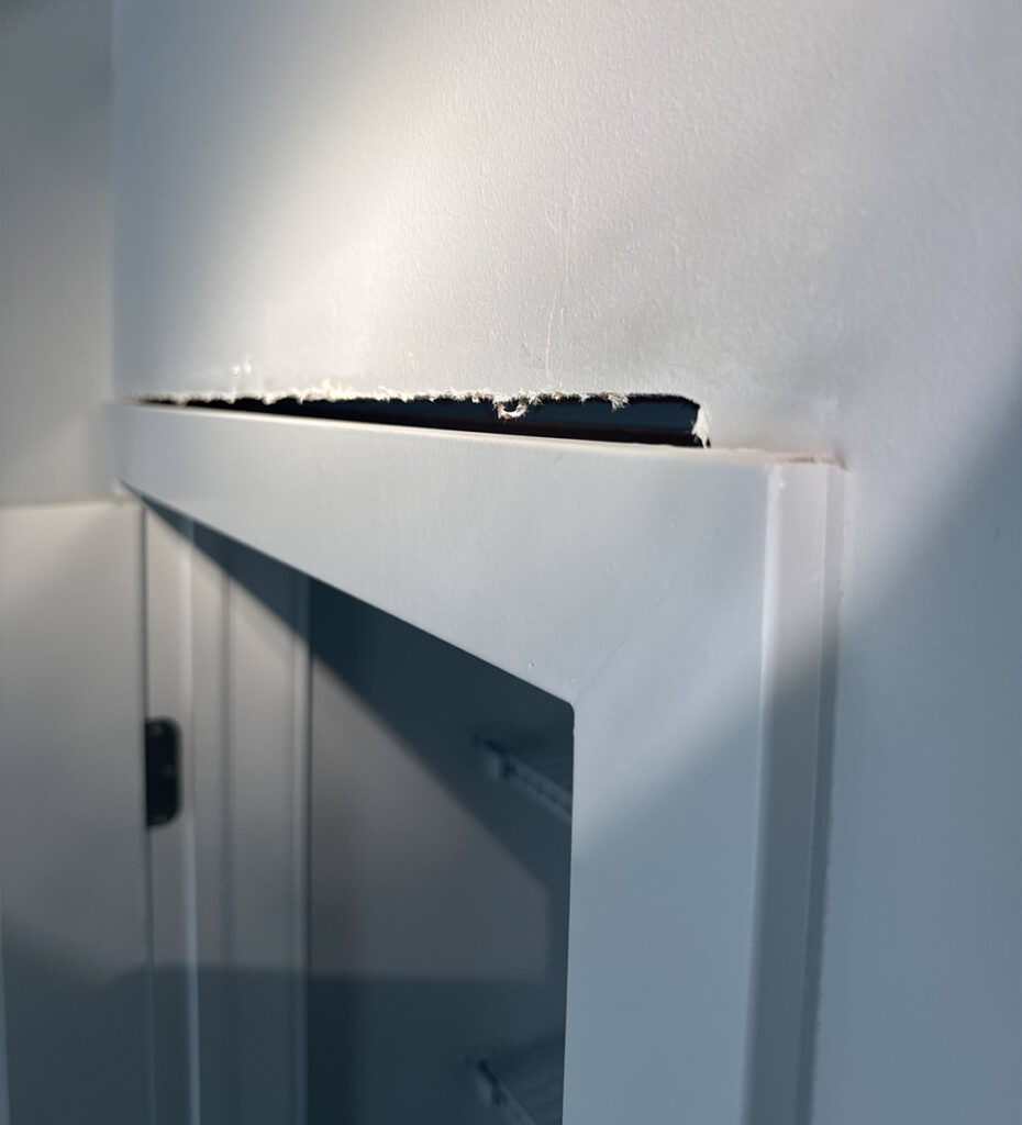Damaged drywall above an interior door frame showing a visible gap, cracked joint, and separation between the wall and door trim.