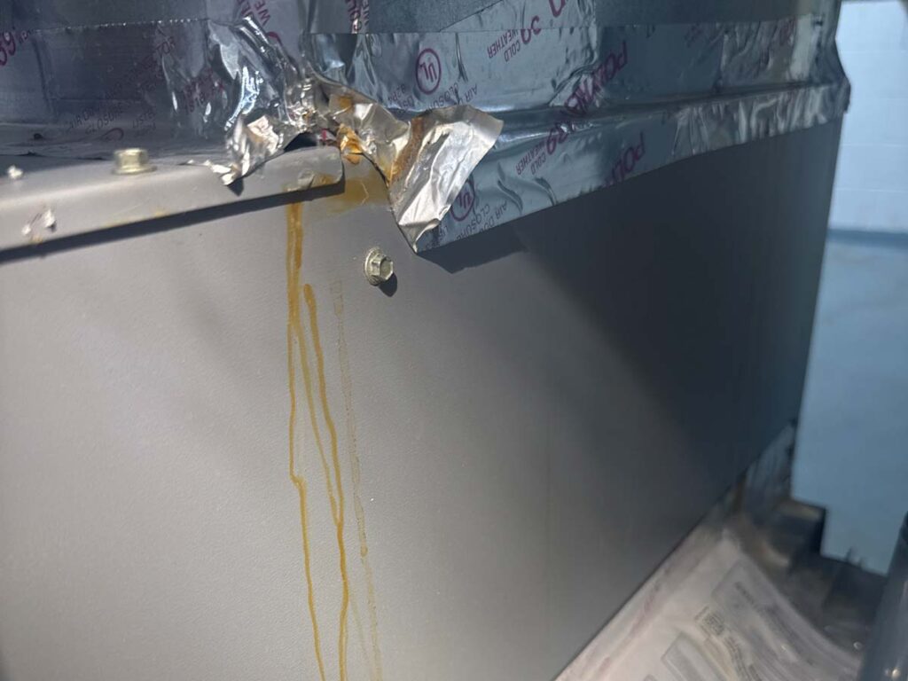 Yellowish-brown residue streaks on an indoor HVAC cabinet below a taped duct connection, showing possible evidence of leakage or moisture.
