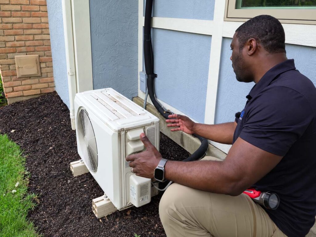Home inspector examining an outdoor ductless mini-split air conditioning unit, including the refrigerant lines and exterior equipment components.