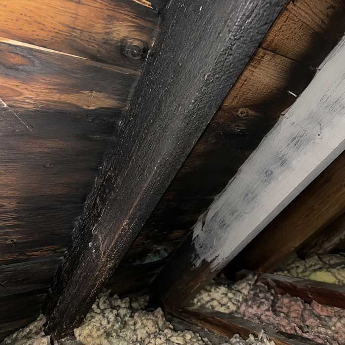 Soot-blackened and painted-over rafters revealing past fire damage during an attic inspection in Columbus, Ohio